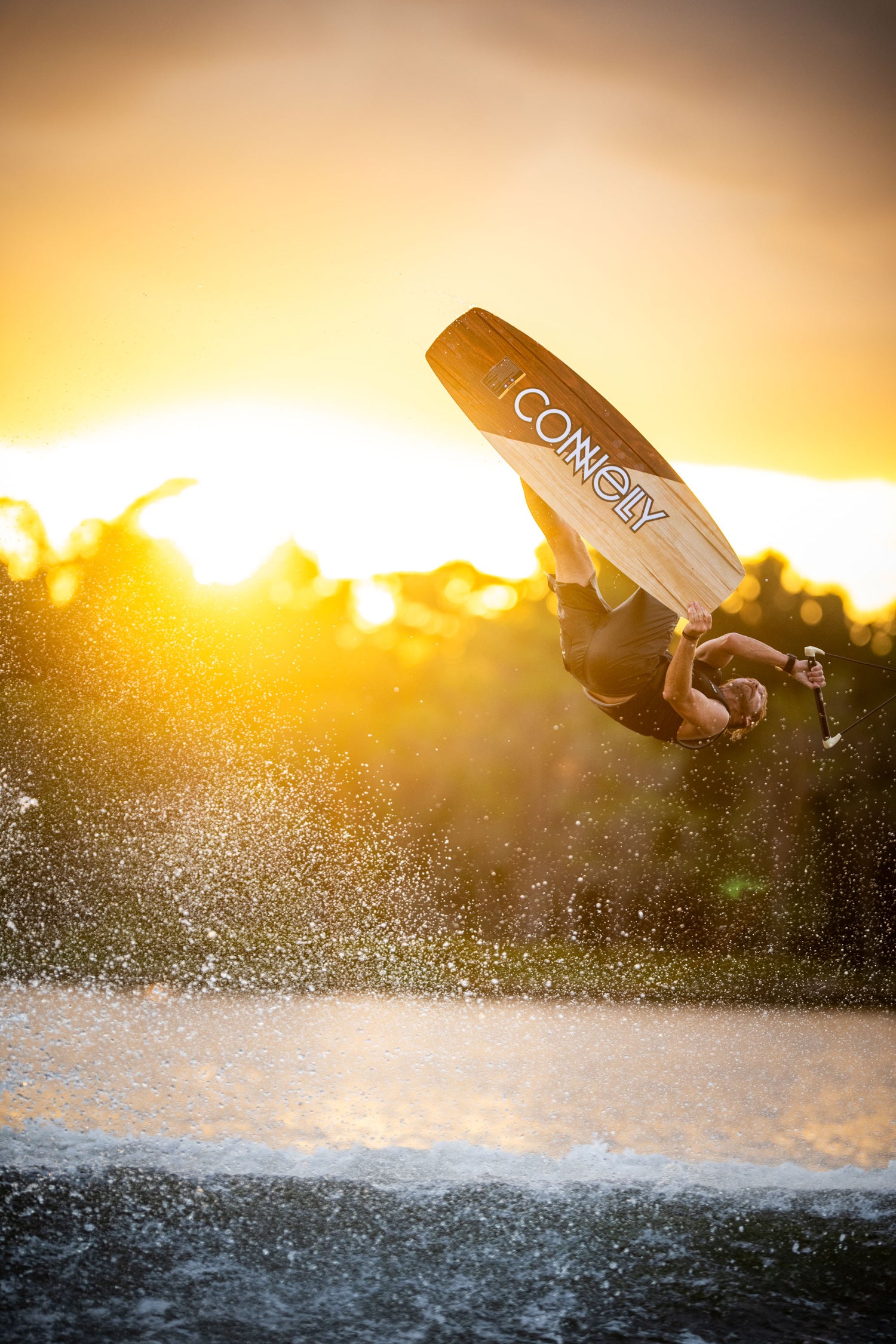 A wakeboarder performs an inverted aerial trick at sunset, showcasing the Connelly Big Easy wakeboard.