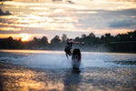 A wakeboarder carves across the water at sunset, creating a spray behind the Connelly Big Easy wakeboard.