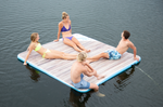 A group relaxing on the Party Cove Dock, a floating inflatable platform with a woodgrain design on a lake.