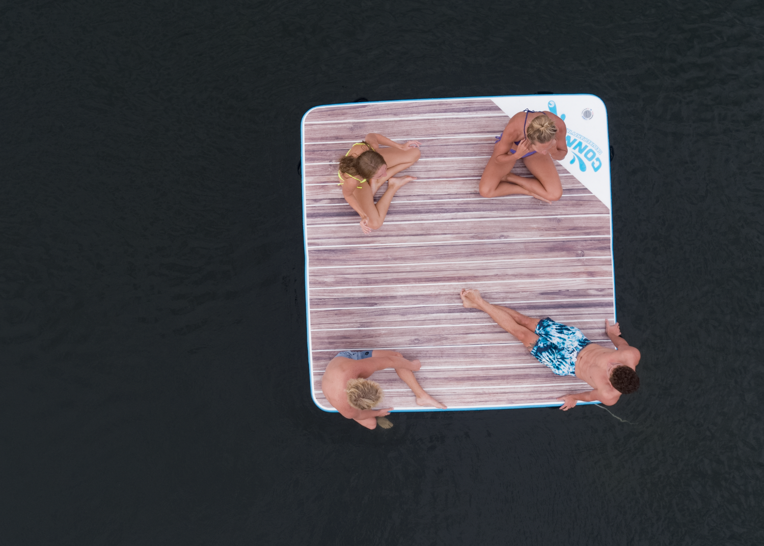 Top-down view of the Party Cove Dock, an 8x8 ft inflatable floating platform with a woodgrain design and blue trim.