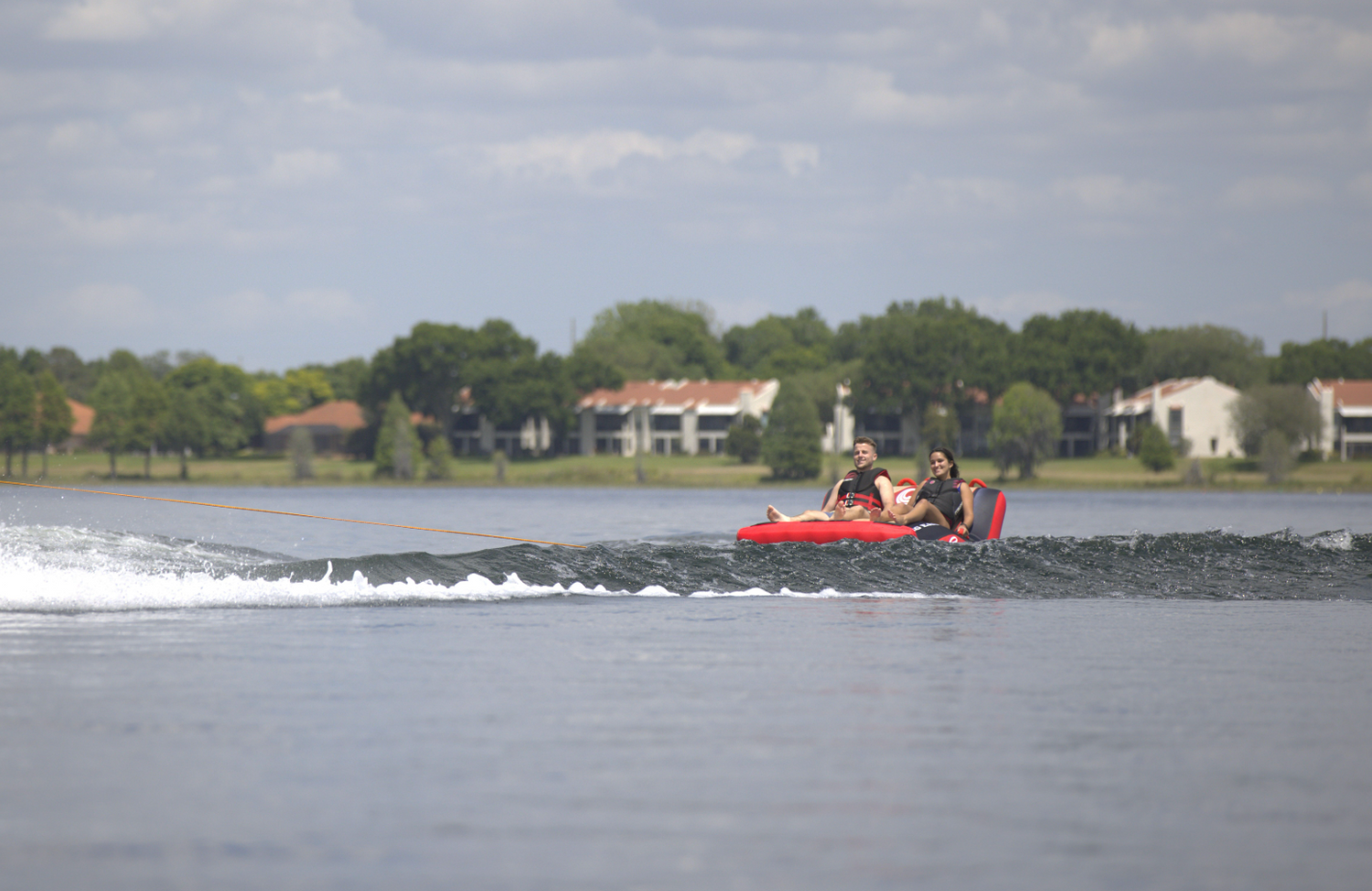 Two riders sit back on the Big Easy 2 towable tube, gliding across the water behind a boat.