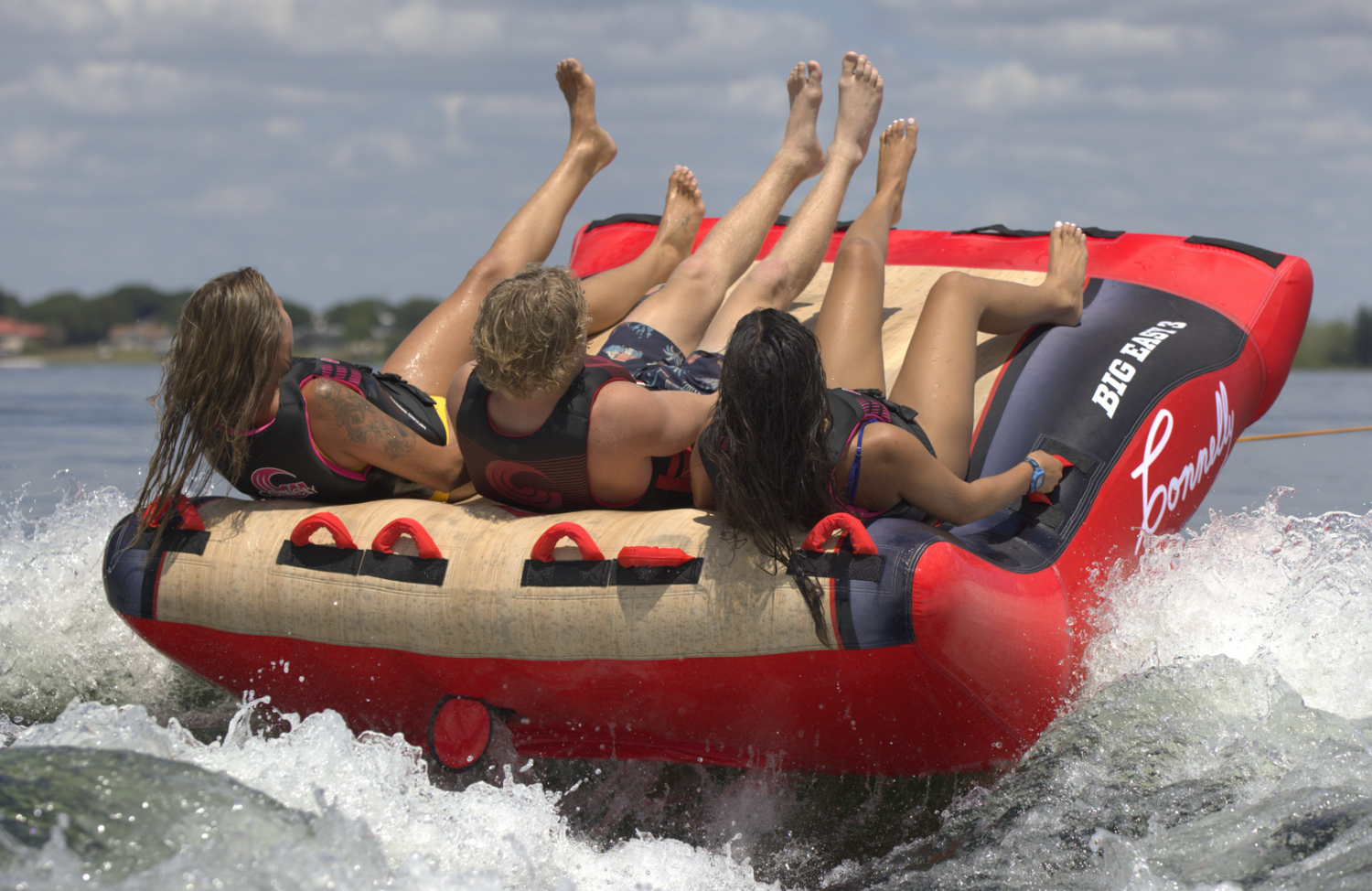 Back view of the Big Easy 3 tube in action as three riders lean back while being pulled across the water, creating a wake.