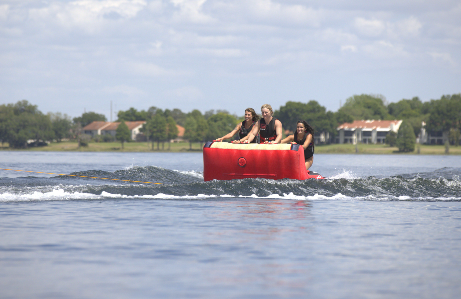 Three riders kneeling on the Big Easy 3 tube while being pulled across the water, gripping the front handles for stability.