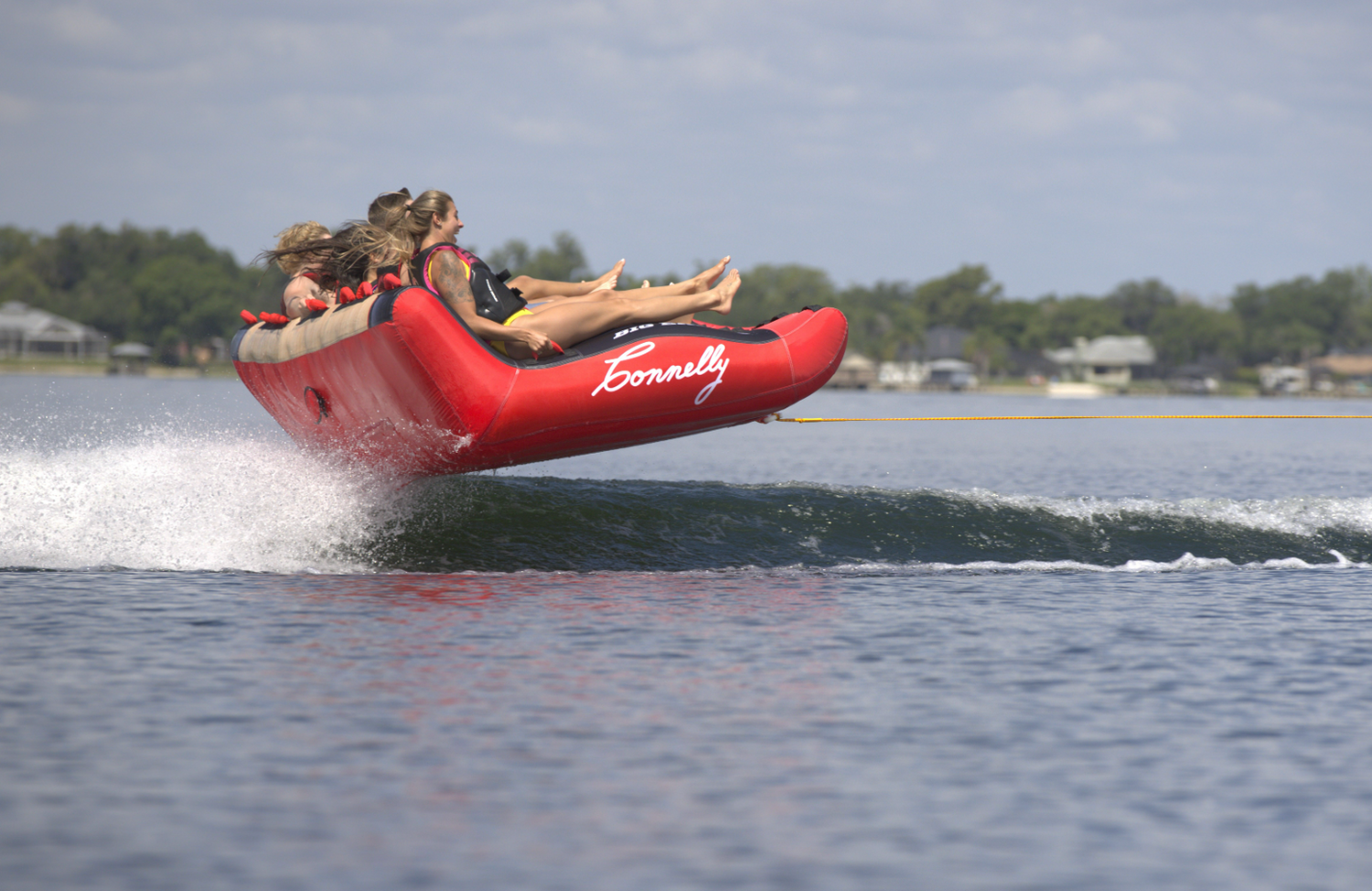 Four riders on Big Easy 4 towable tube, gripping the cushioned backrest as they glide across the water.