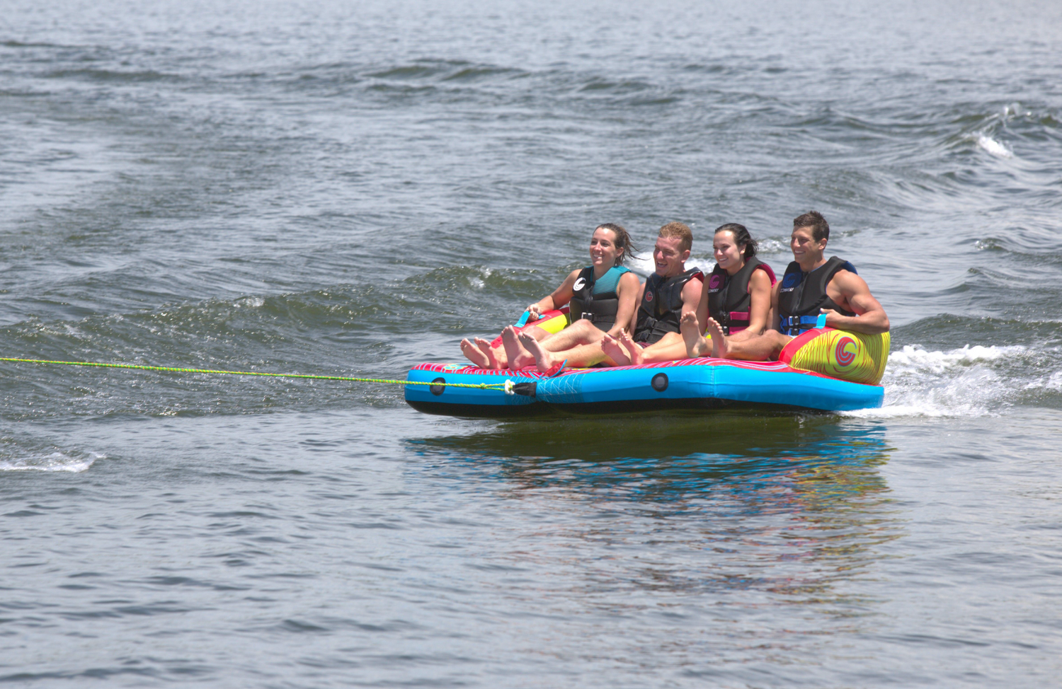 Fun 4 towable tube with four riders gripping handles and gliding across the water behind a boat.