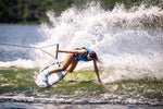 Wakeboarder carving a wave on the Lotus wakeboard, leaning into the water with one hand while creating a large splash.