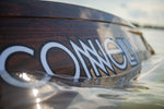 Close-up of the Connelly Big Easy wakeboard floating on the water, with droplets highlighting its sleek woodgrain design.