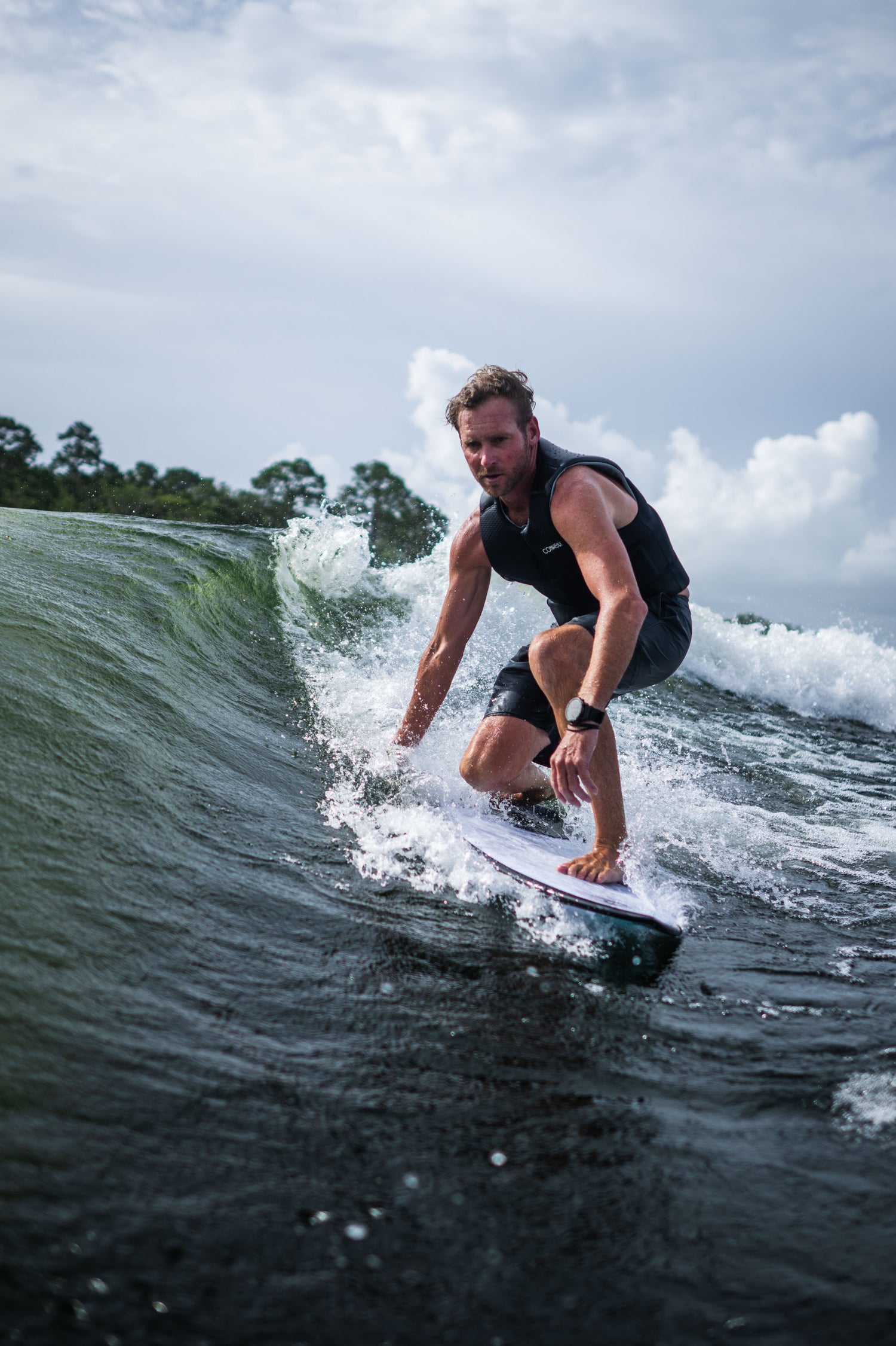 A male surfer in a black life vest carves through a wave while riding the Seer wakesurf board.