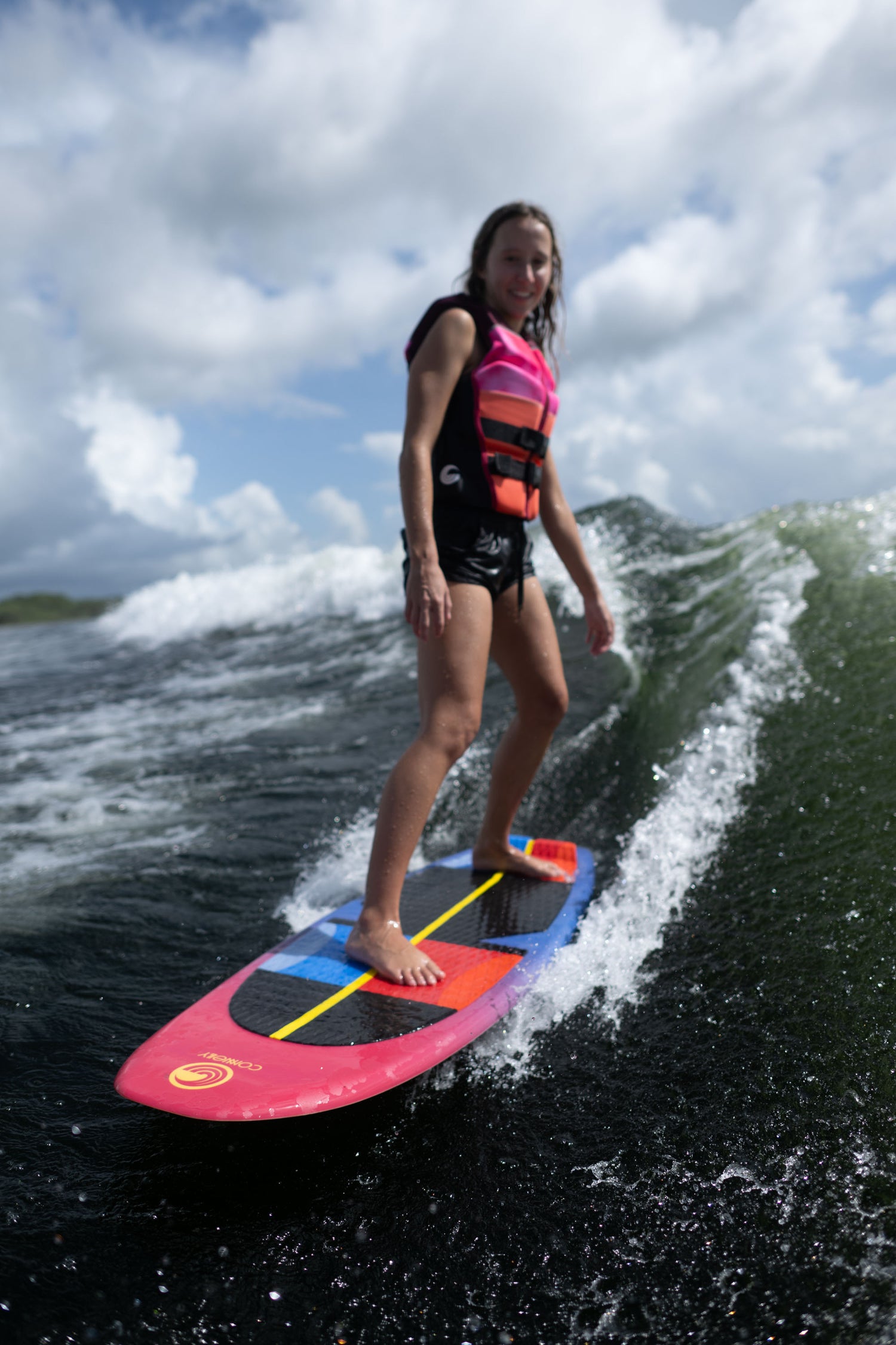 Woman riding the SPARK wakesurf board on a wave, balancing with bent knees and arms extended.