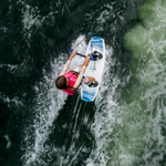 A young rider in a pink vest wakeboarding on the Surge, gripping a handle while carving through the water.