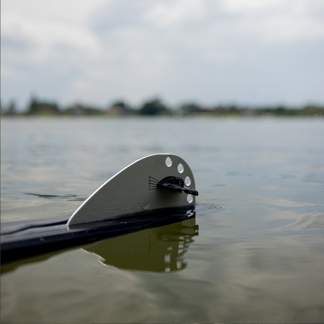 Close-up of adjustable aluminum fin on 2024 Women's Concept waterski, partially submerged in calm water.