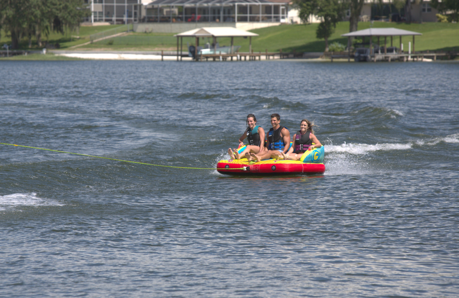 Fun 3 towable tube with three riders sitting upright, holding handles, and gliding across the water on a bright inflatable.