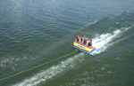 Fun 4 towable tube with four riders, a visible wake trail, and a tow rope extending forward.