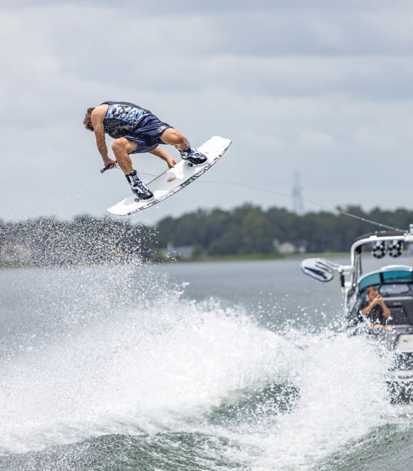 Wakeboarder performs an aerial trick wearing the Connelly SL wakeboard boots, with a boat and waves in the background.