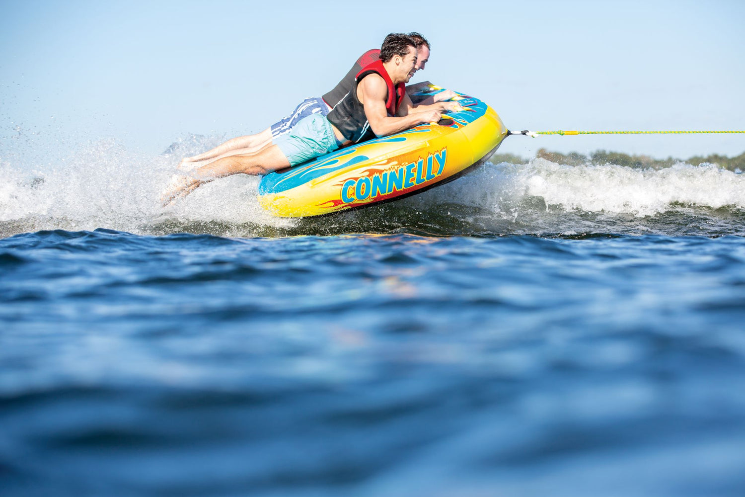 The Hot Rod towable tube with two riders gripping handles and skimming across the water behind a boat.