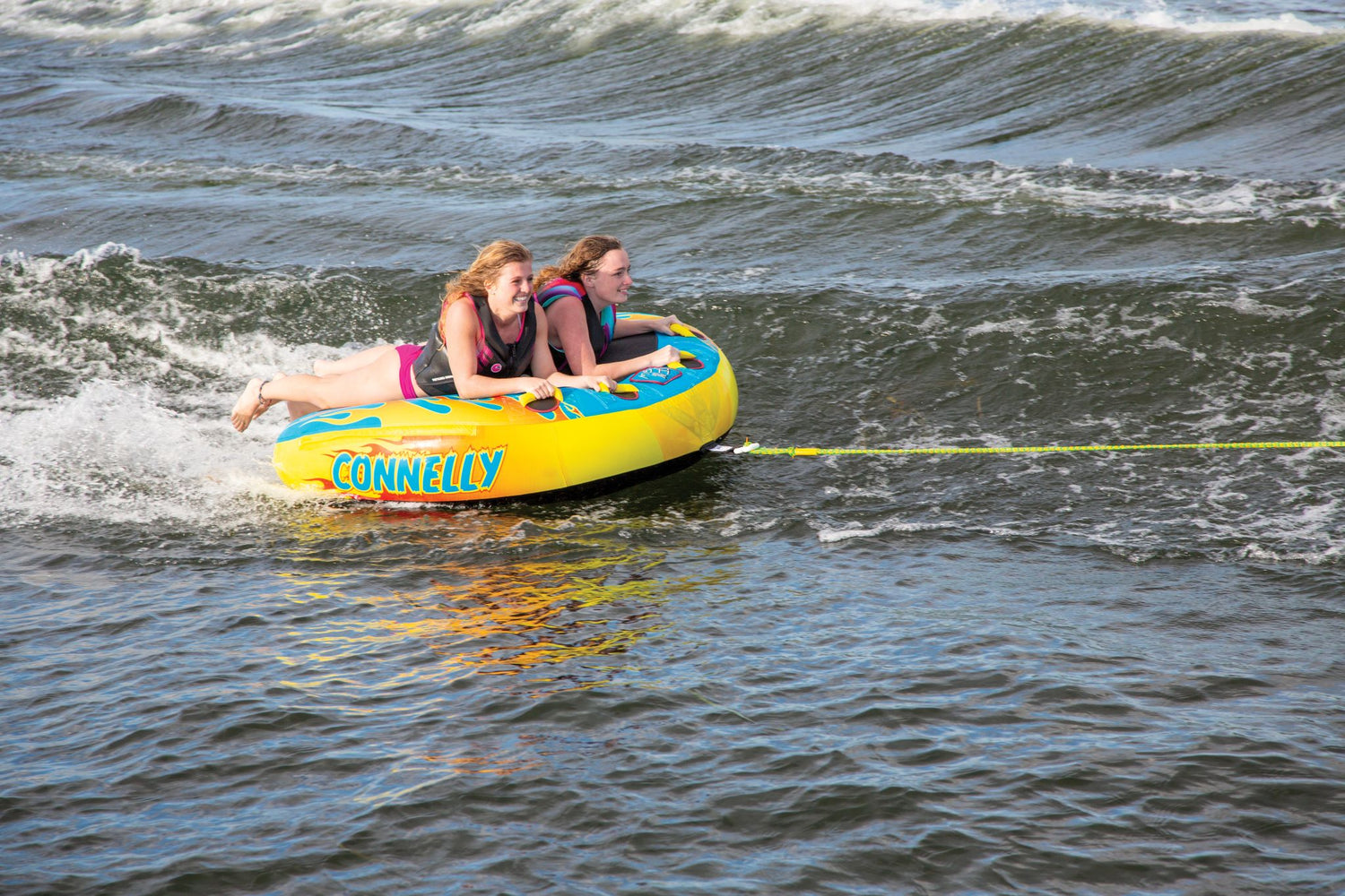 The Hot Rod towable tube with two riders lying flat and holding on tightly while being pulled across the water.