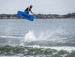 Wakeboarder performs an aerial trick over the water using the Connelly Reverb wakeboard, creating a spray from the wake.