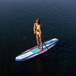 A woman in a yellow swimsuit paddles on the Drifter iSUP on calm water.