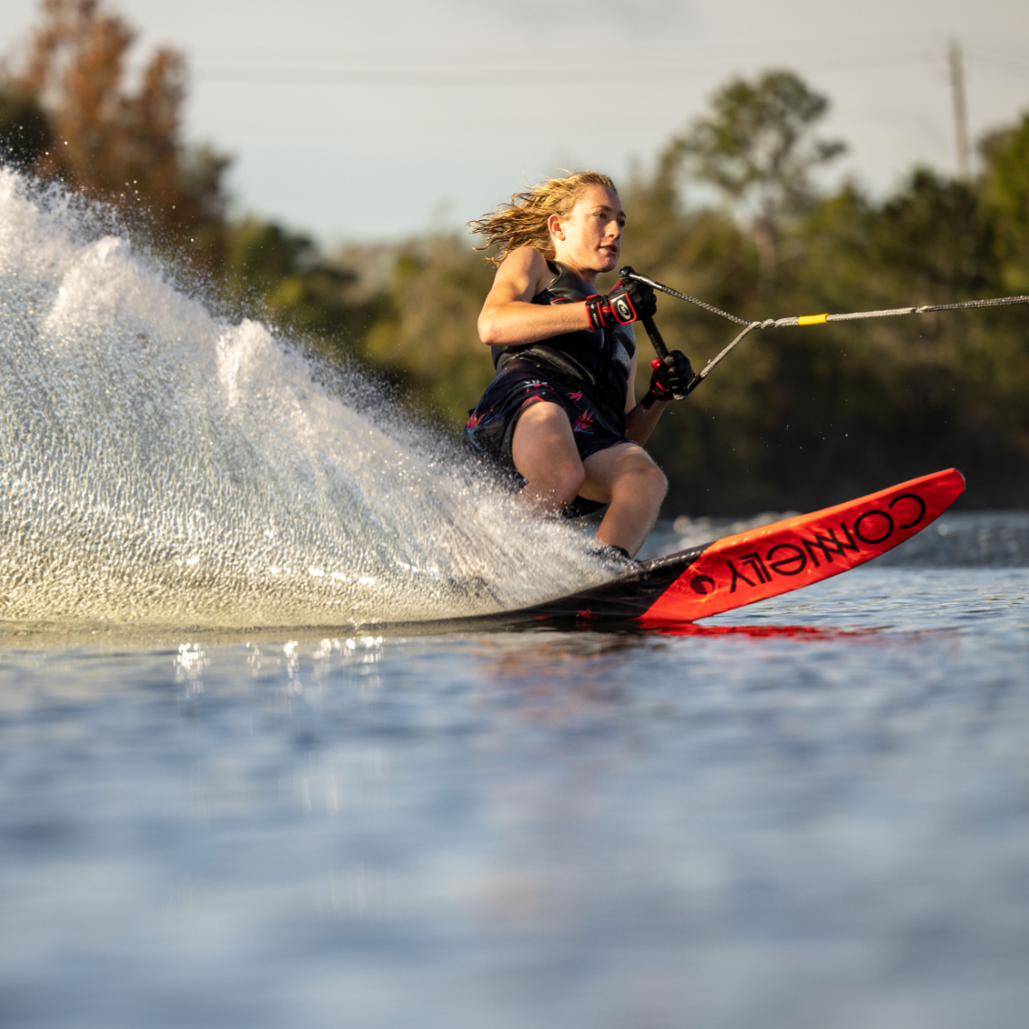 Close-up of the 2022 Men's Concept waterski tip cutting through water, with a bold red design and black Connelly logo.