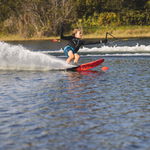 A female skier carves on the 2022 Men's Concept waterski, leaning into a turn with a spray of water and a firm grip.