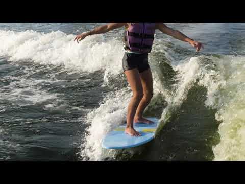 A child surfing on the 2024 Dash Kid’s Board, balancing on a wave with the vibrant orange and yellow board beneath them.